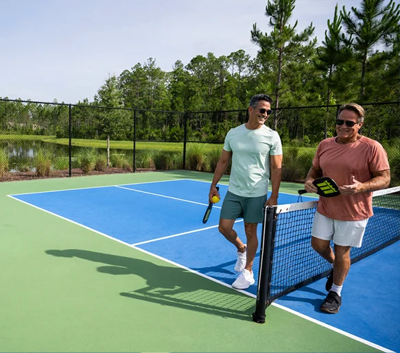 Two men laughing at the net on a pickleball court at Tributary.
