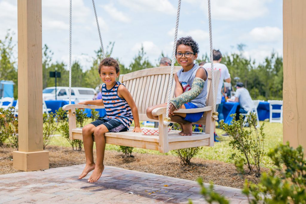 2 kids smiling on swing at the Tributary Model Home Event park