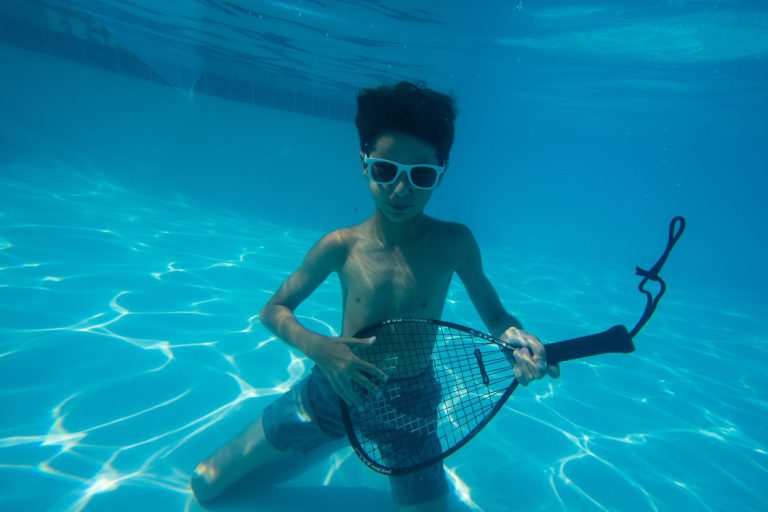 boy playing the air guitar on racket in pool
