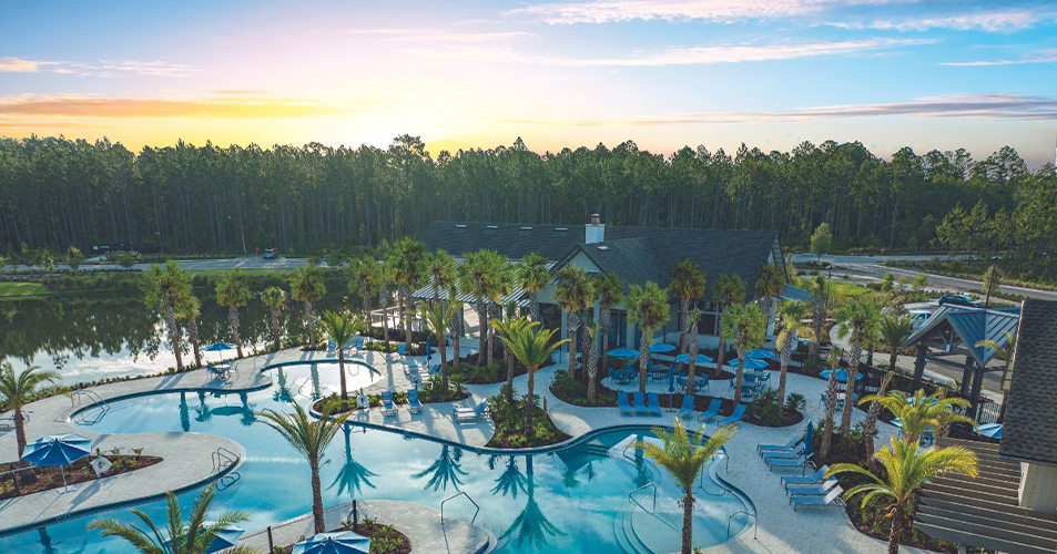 Aerial view of pool and clubhouse beside lake at sunset