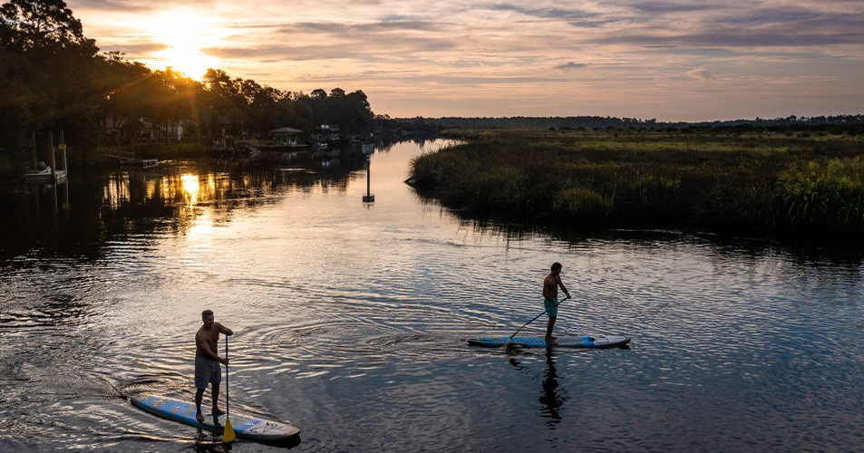 Two people paddleboarding on river at sunset