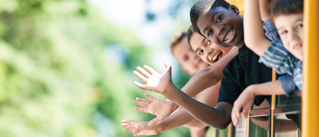 Smiling children waving from the windows of a yellow school bus