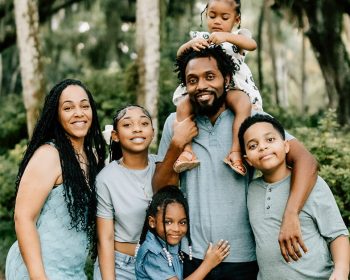 Family of six posing together in park with trees