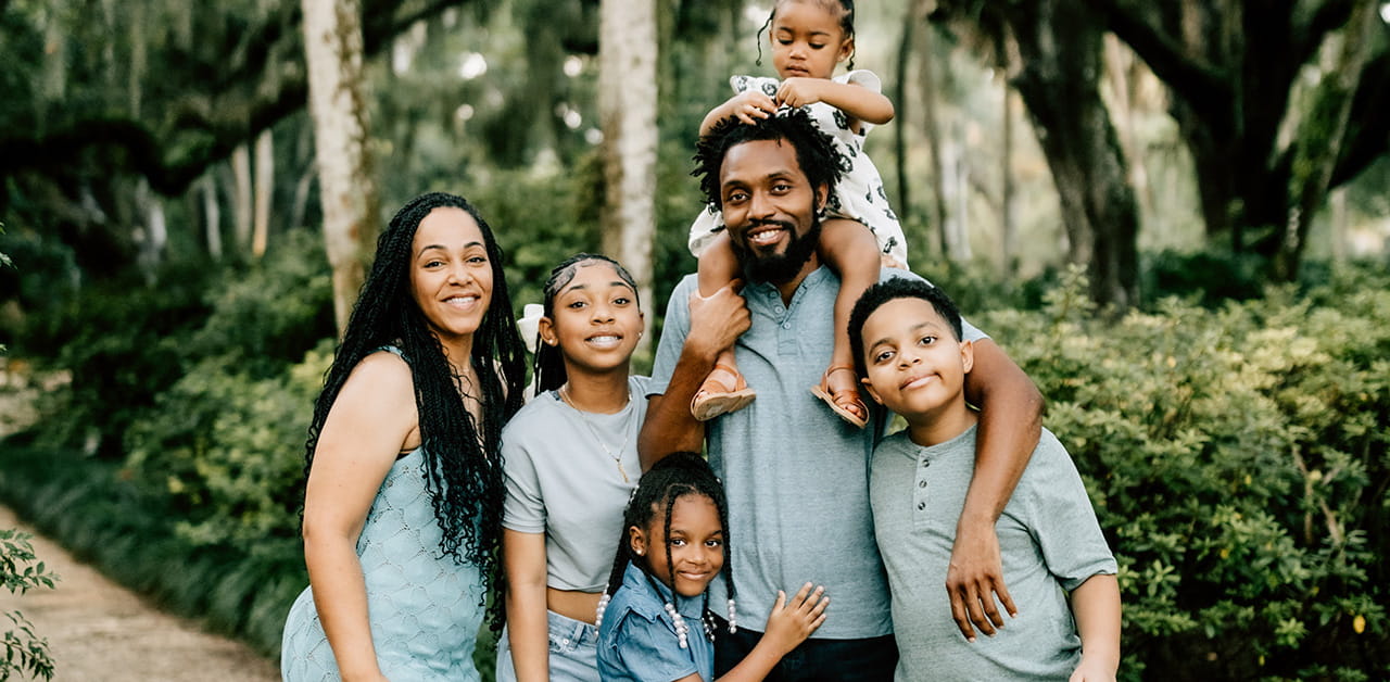 Family of six posing together in park with trees