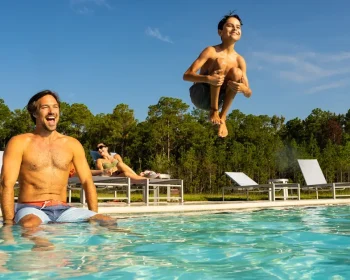 Father and son enjoy quality time at a luxury resort pool with pristine facilities and scenic forest views on a sunny day.